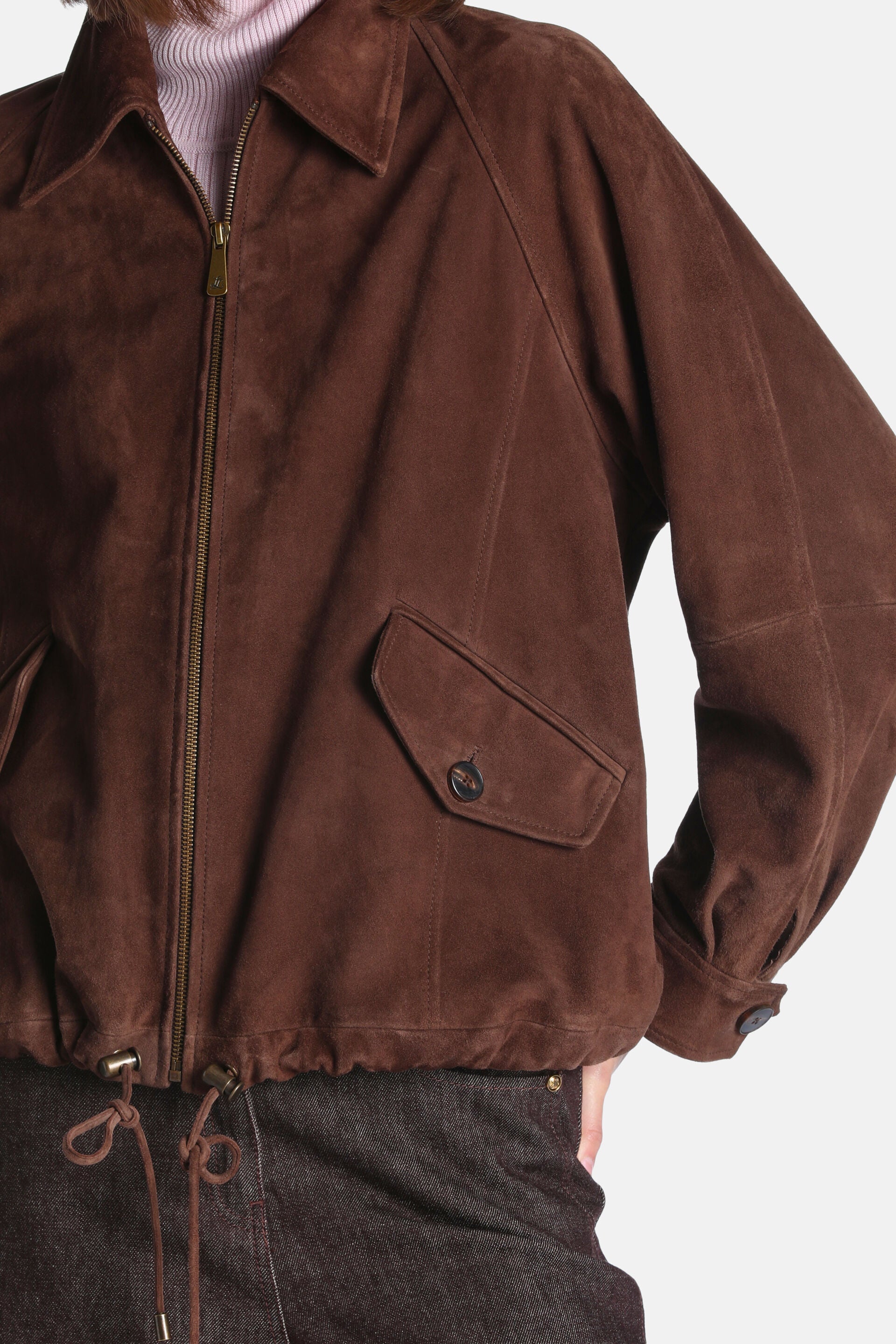 Brown suede bomber jacket with a pointed collar, gold-toned full-zip front, flap pocket with dark button, drawstring hem, and