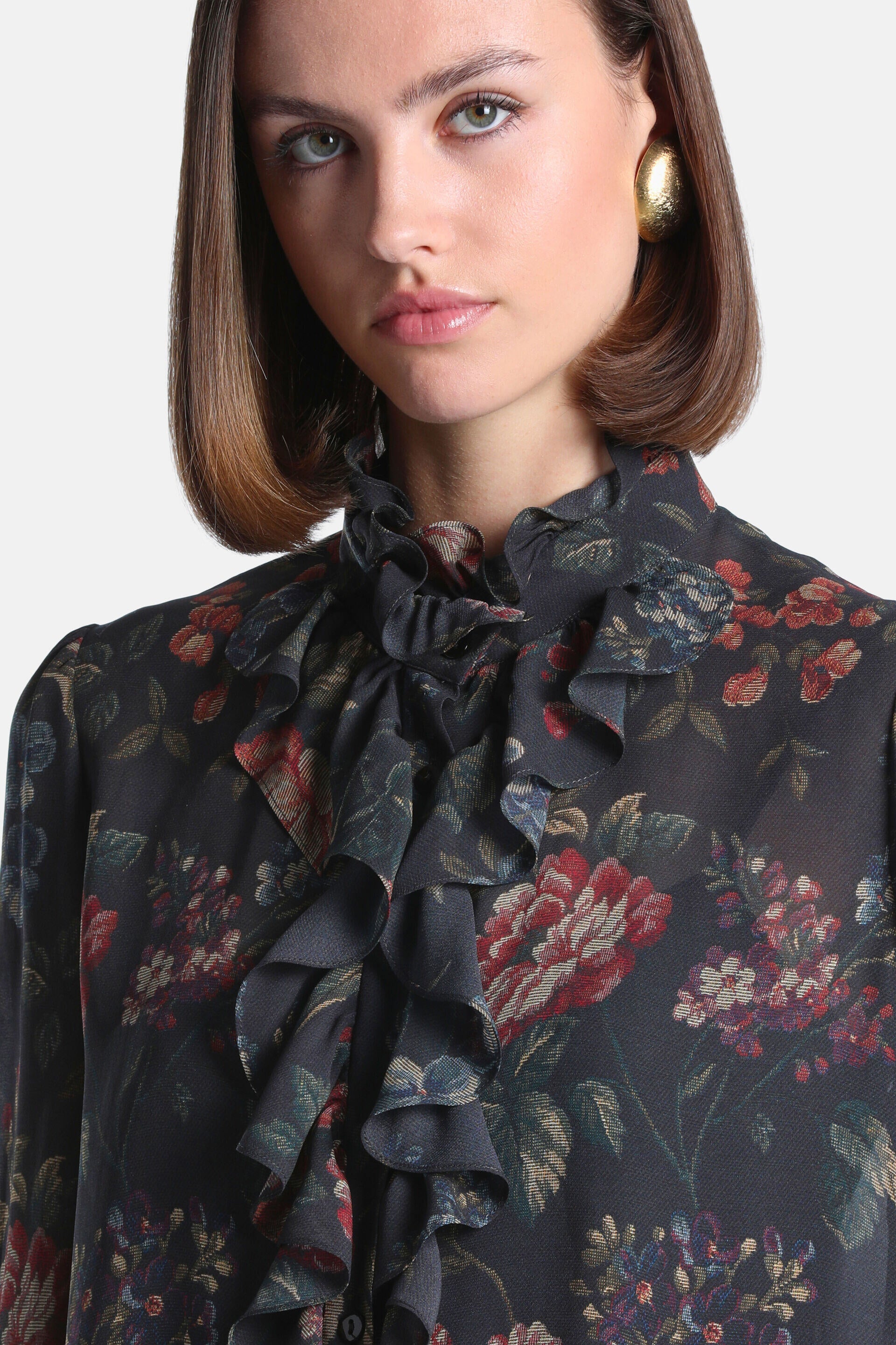 Dark grey floral blouse with a high ruffled collar and ruffled front placket. Woven red, blue, and green floral patterns.