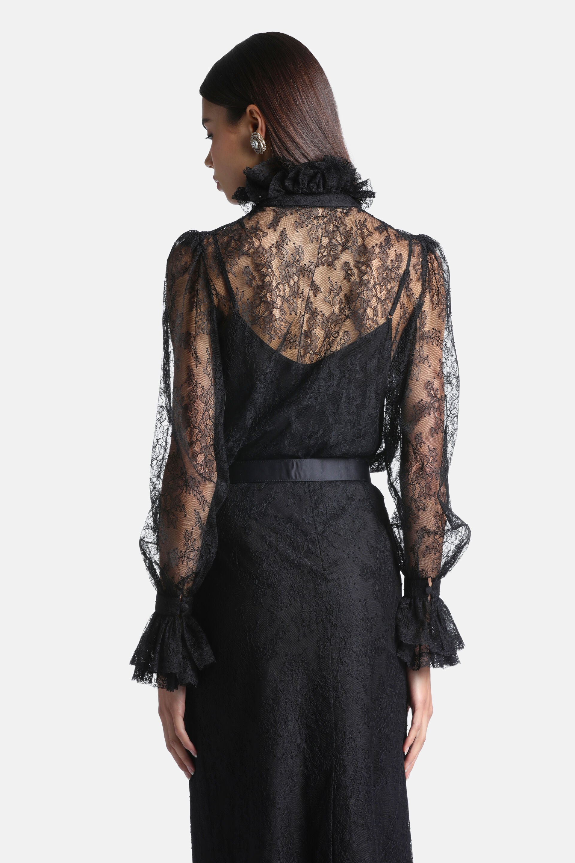Black sheer lace shirt with a high ruffled collar, long puffed sleeves, and ruffled cuffs with button details. Features a flo