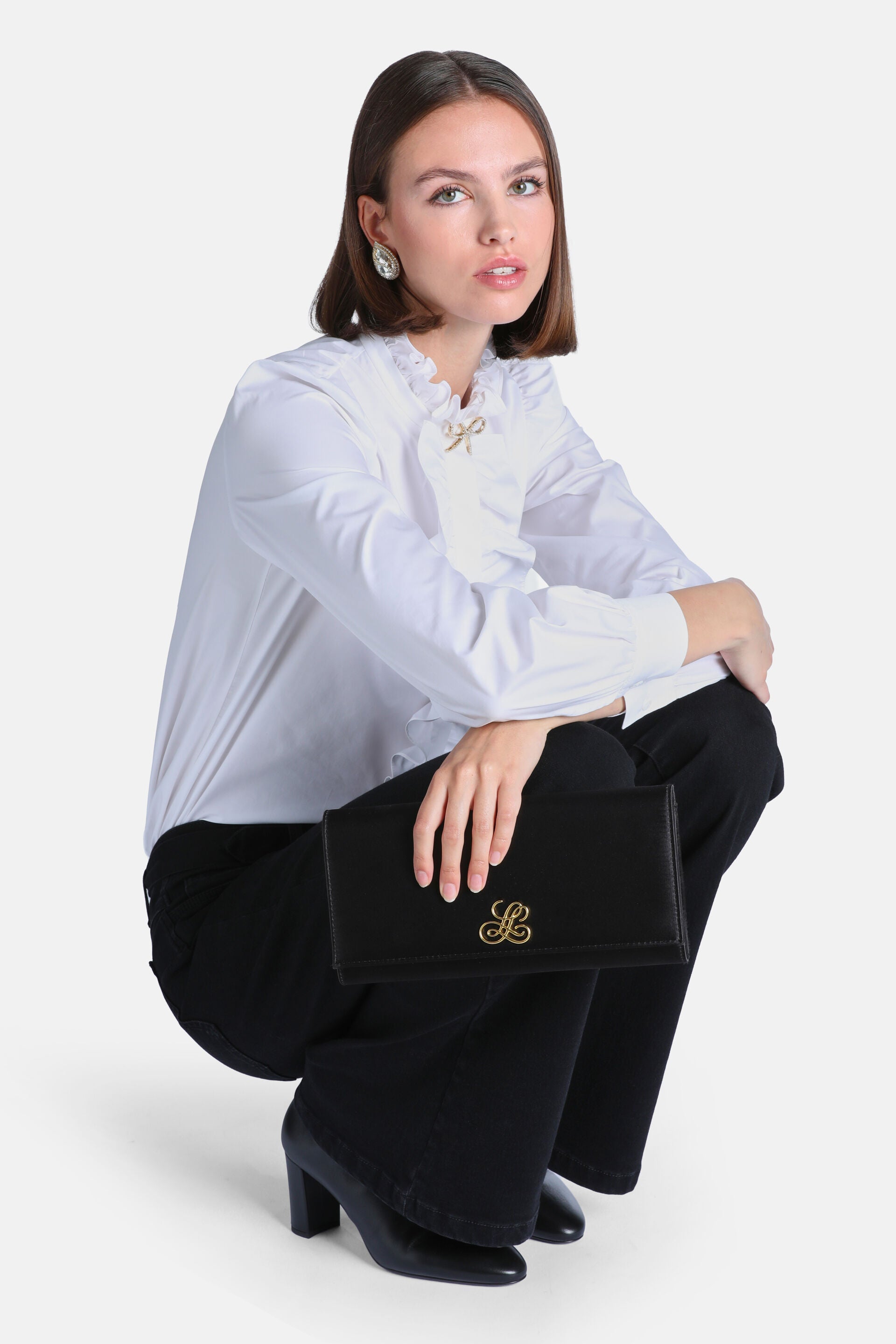 White long-sleeved shirt with a ruffled stand-up collar and a gold-toned bow brooch on the chest.