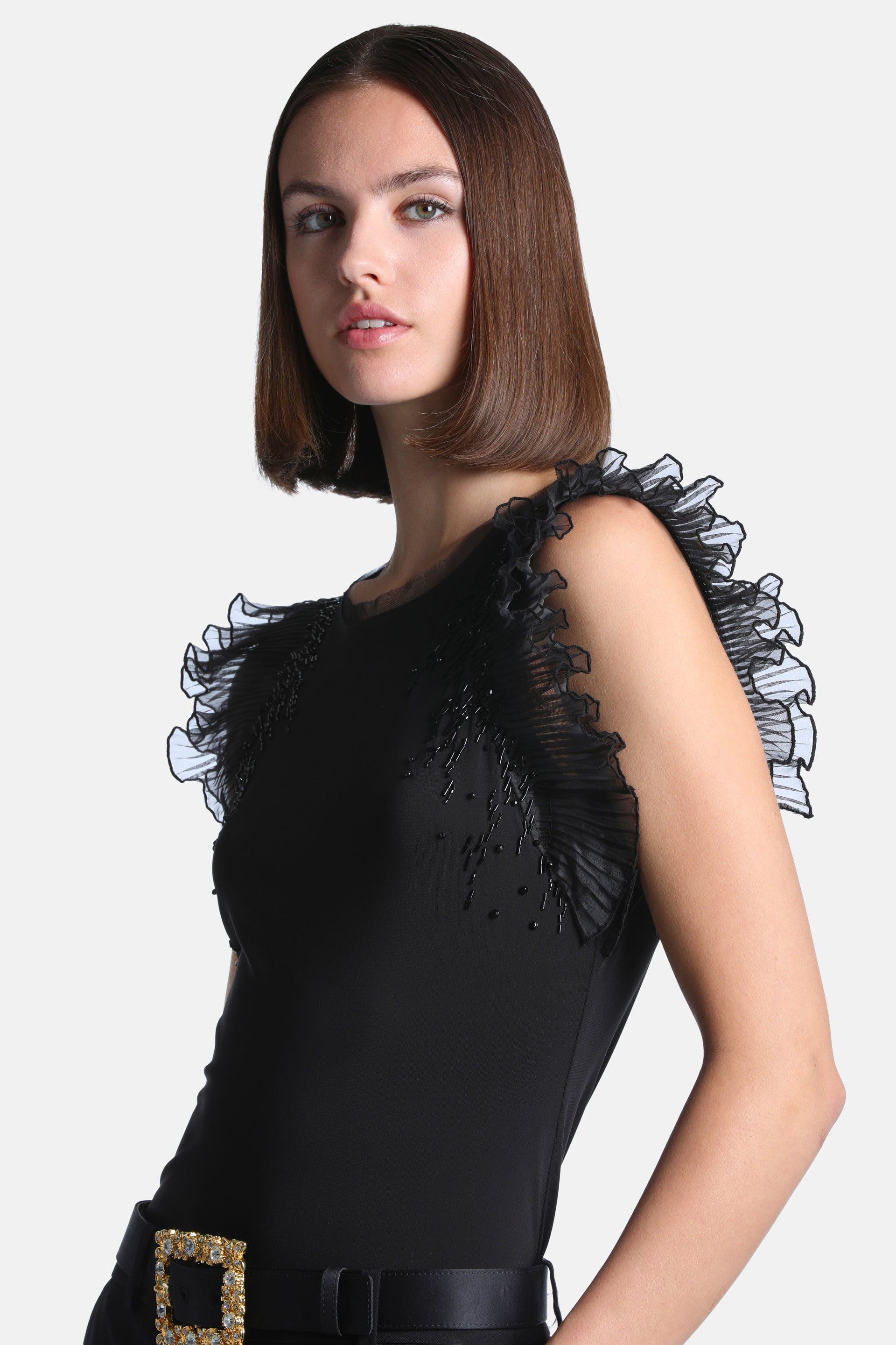 Black top with a round neck, sheer black ruffled cap sleeves with light edges, and black beaded embellishments on the front.