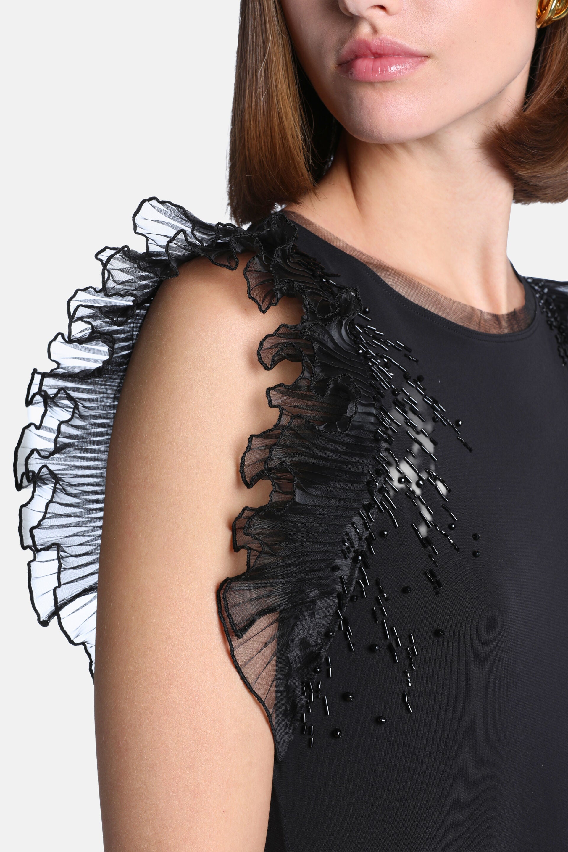 Black top with a sheer-trimmed round neckline. It has ruffled sheer sleeves and scattered black round and bugle bead embellis