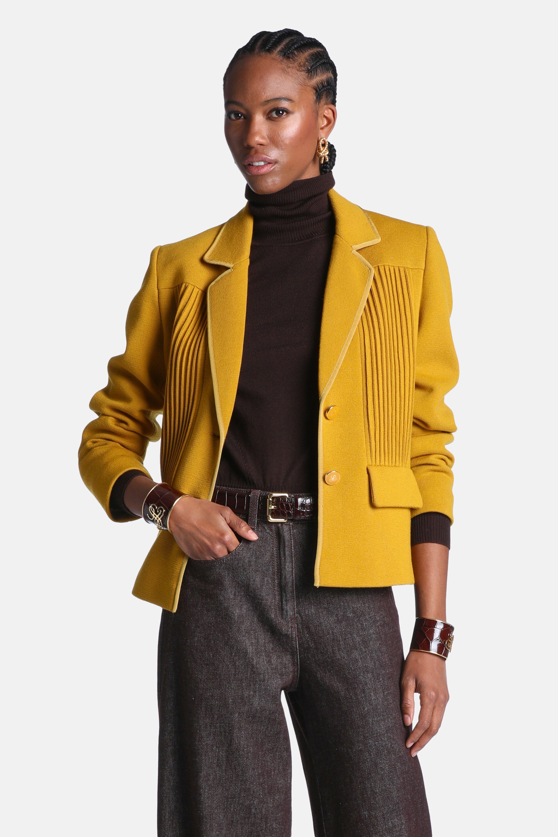 Mustard yellow cropped jacket with notched lapels, two front buttons, two flap pockets, and vertical tucks on the front. Ligh
