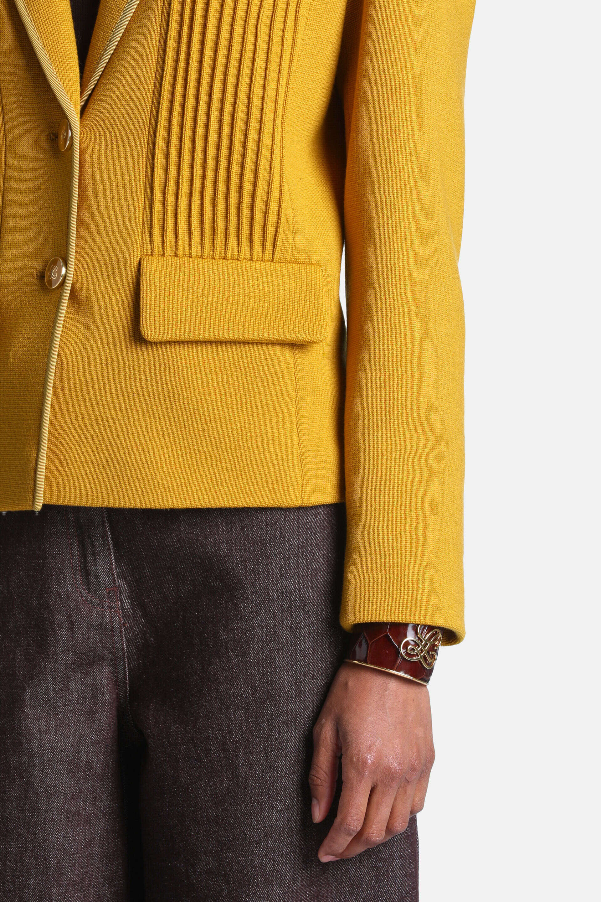 Mustard yellow knit jacket with vertical pleats on the right front, light piping, two gold-toned buttons, and a flap pocket.