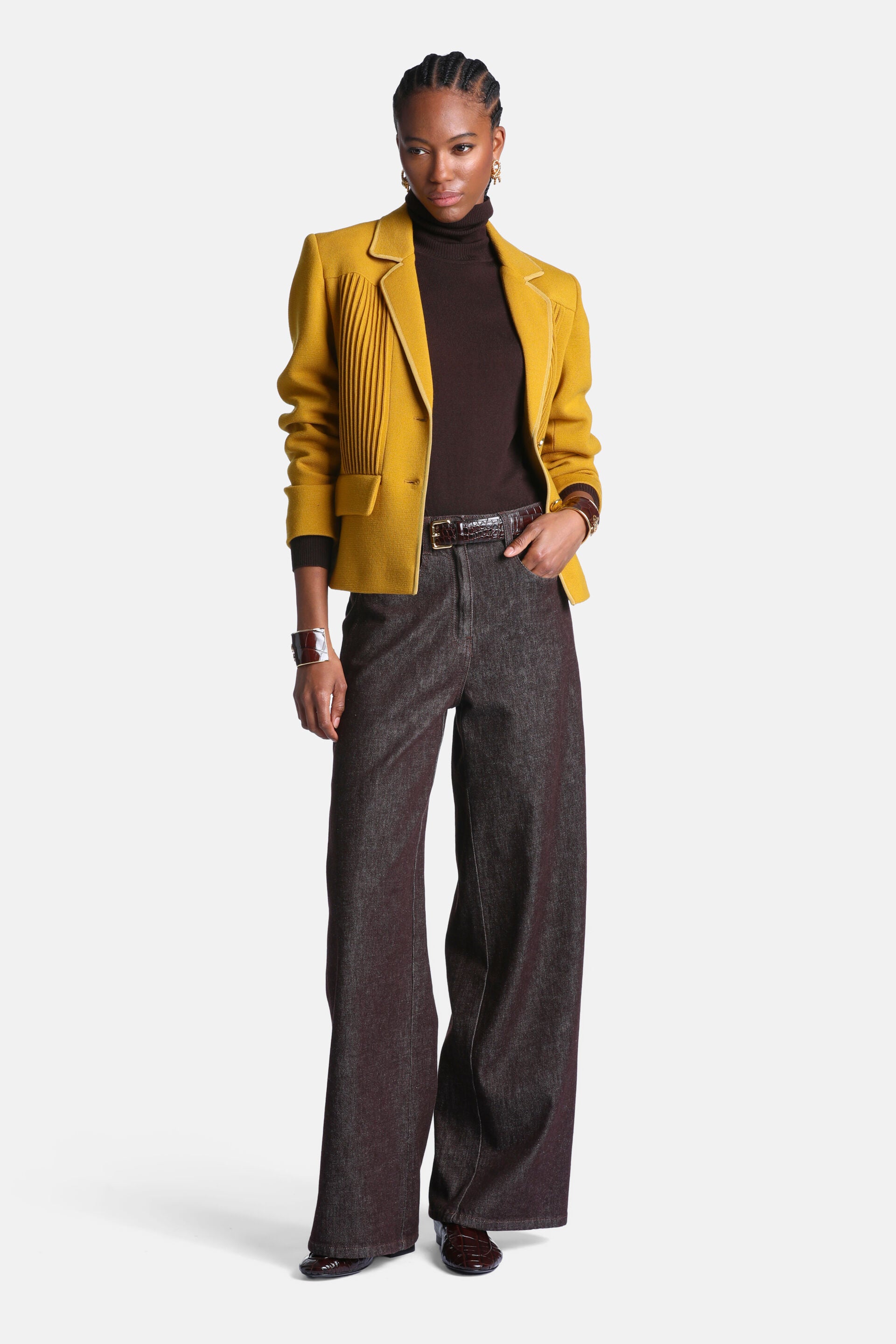 Mustard yellow cropped jacket with notched lapels, lighter trim, vertical pleats on the left front, and a gold-toned button.