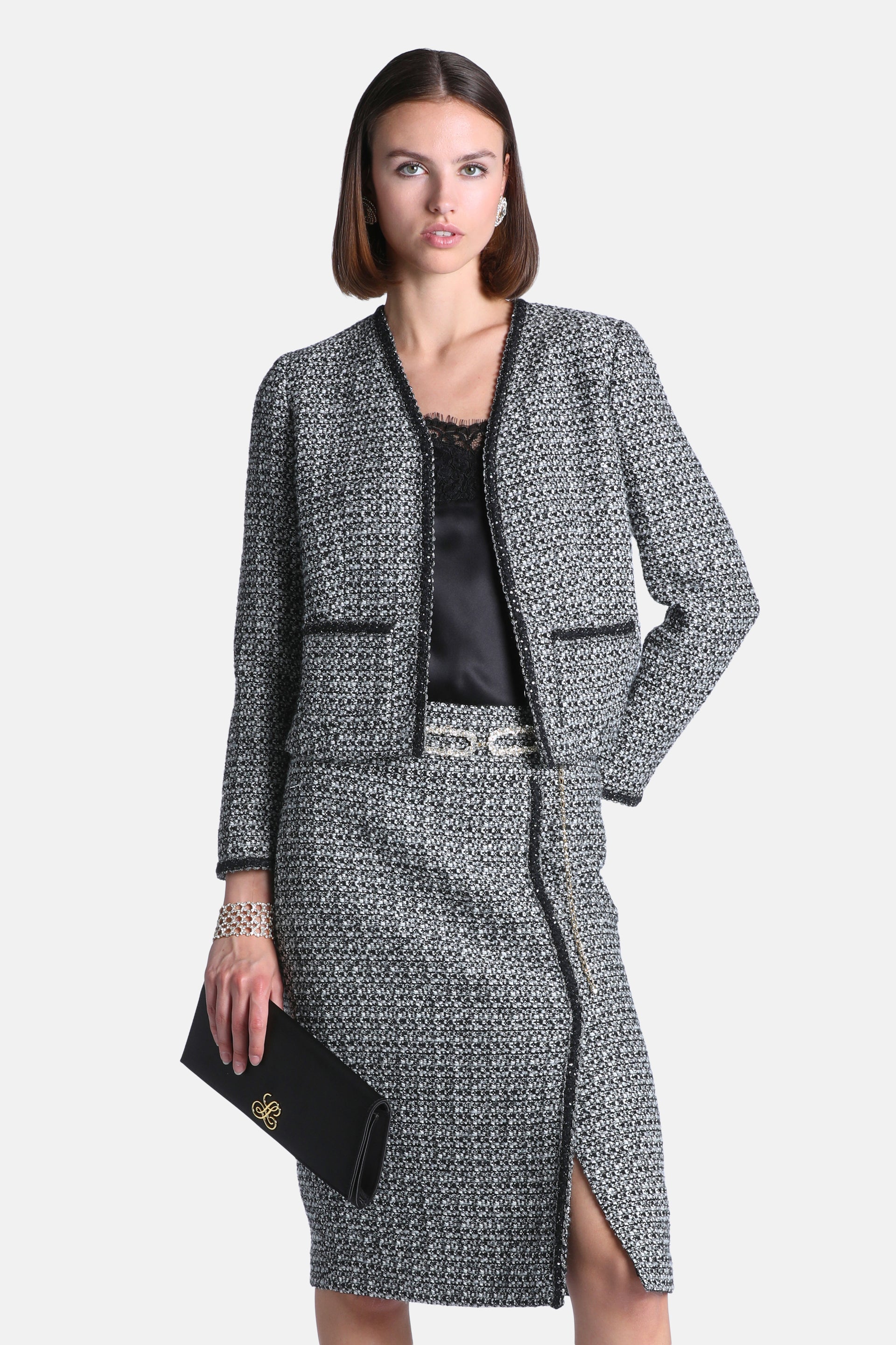 Black and cream tweed jacket with a collarless V-neck, black embellished trim, and two front patch pockets.