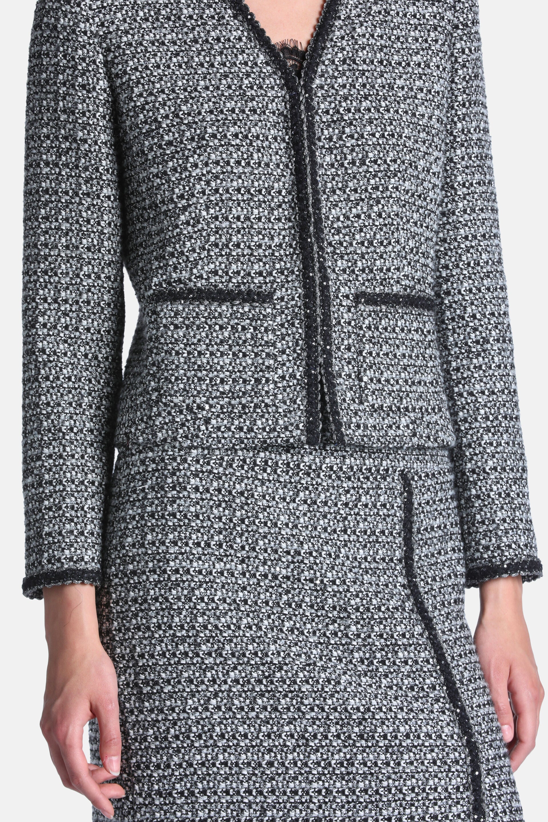 Black and cream speckled tweed jacket with a V-neck, collarless design, two front flap pockets, and black sequined trim.