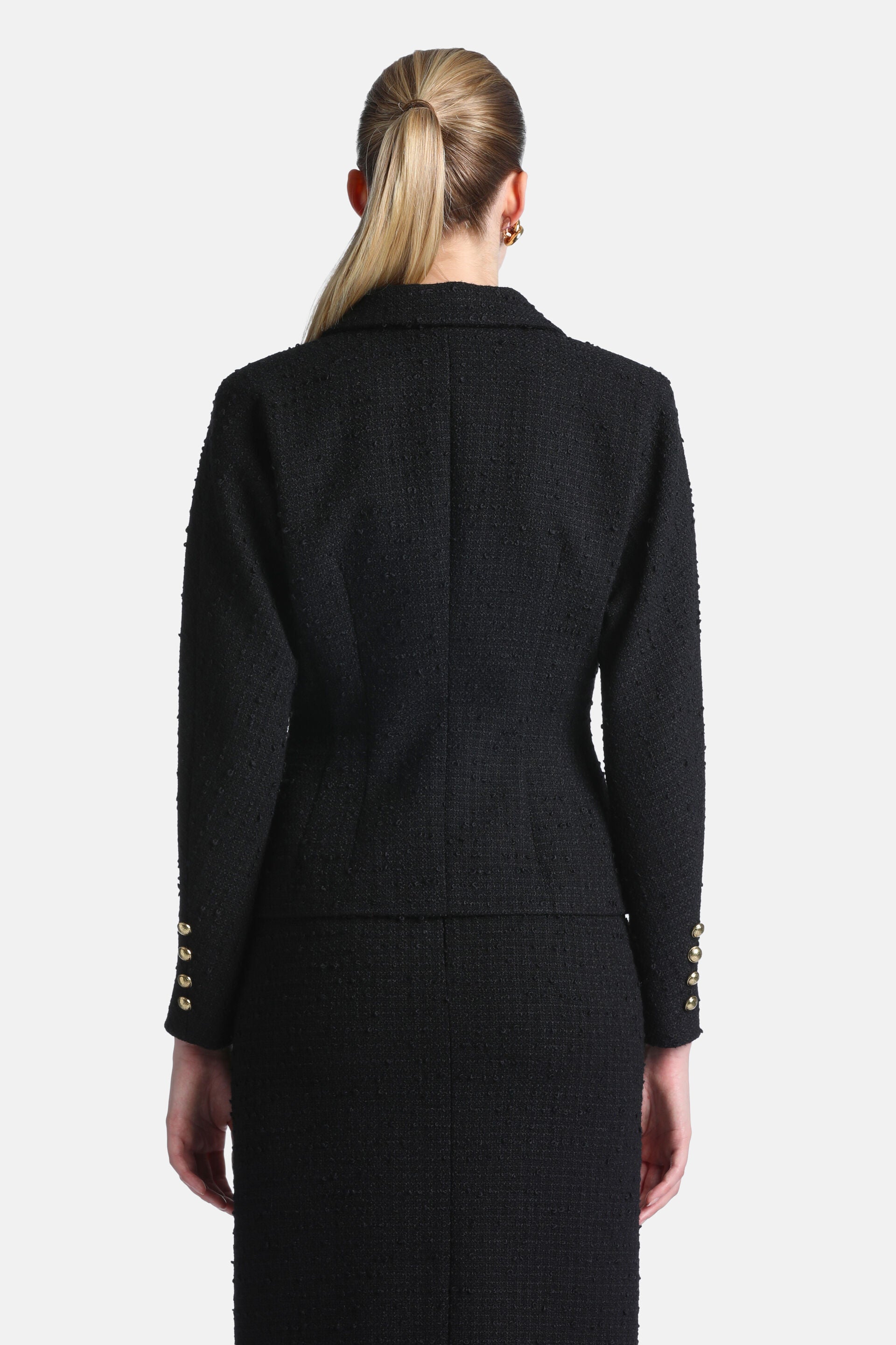 Black tweed jacket, seen from the back, with a textured weave. Each sleeve cuff features four gold-toned buttons.