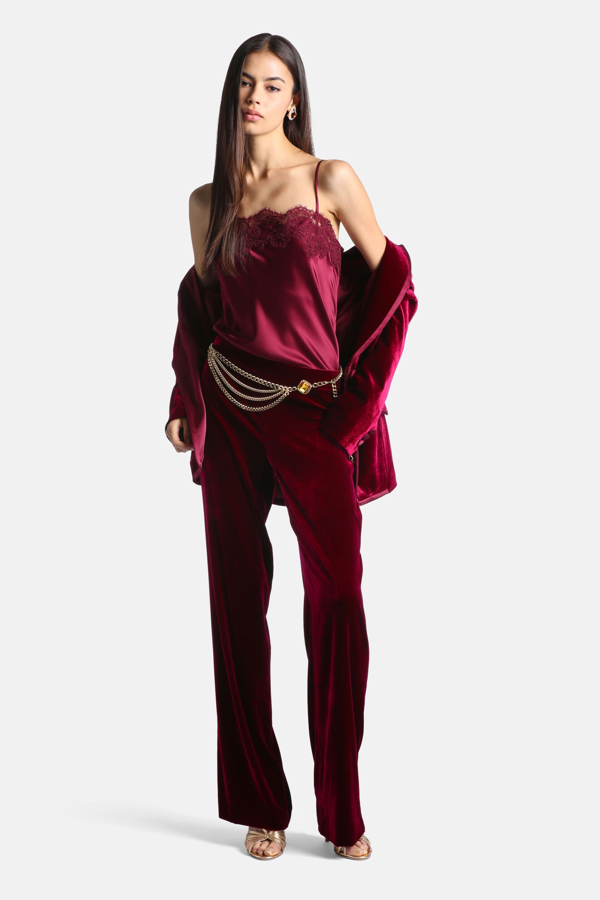 Burgundy velvet blazer and wide-leg pants set, with a matching satin camisole featuring lace trim. Gold-toned chain belt with