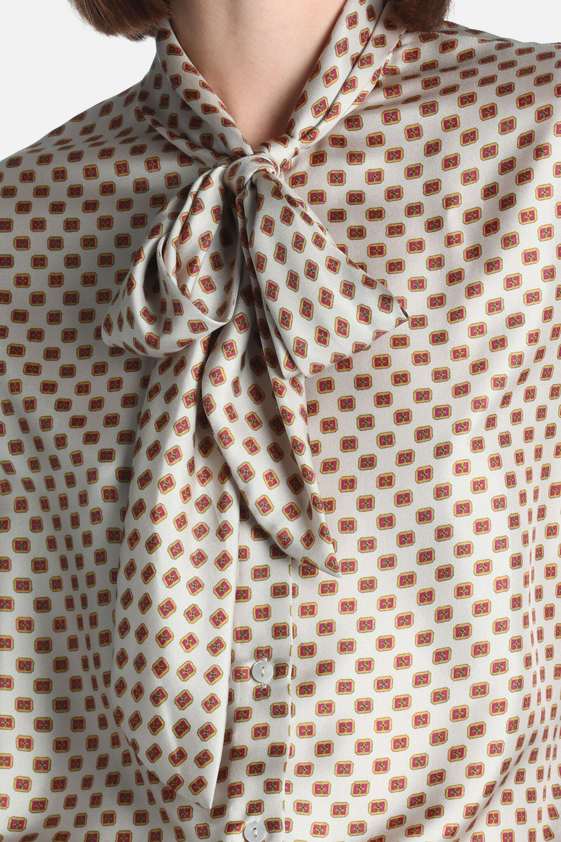 Cream silk shirt with a pussy-bow tie, featuring a pattern of small red and gold-toned square motifs. White buttons visible.