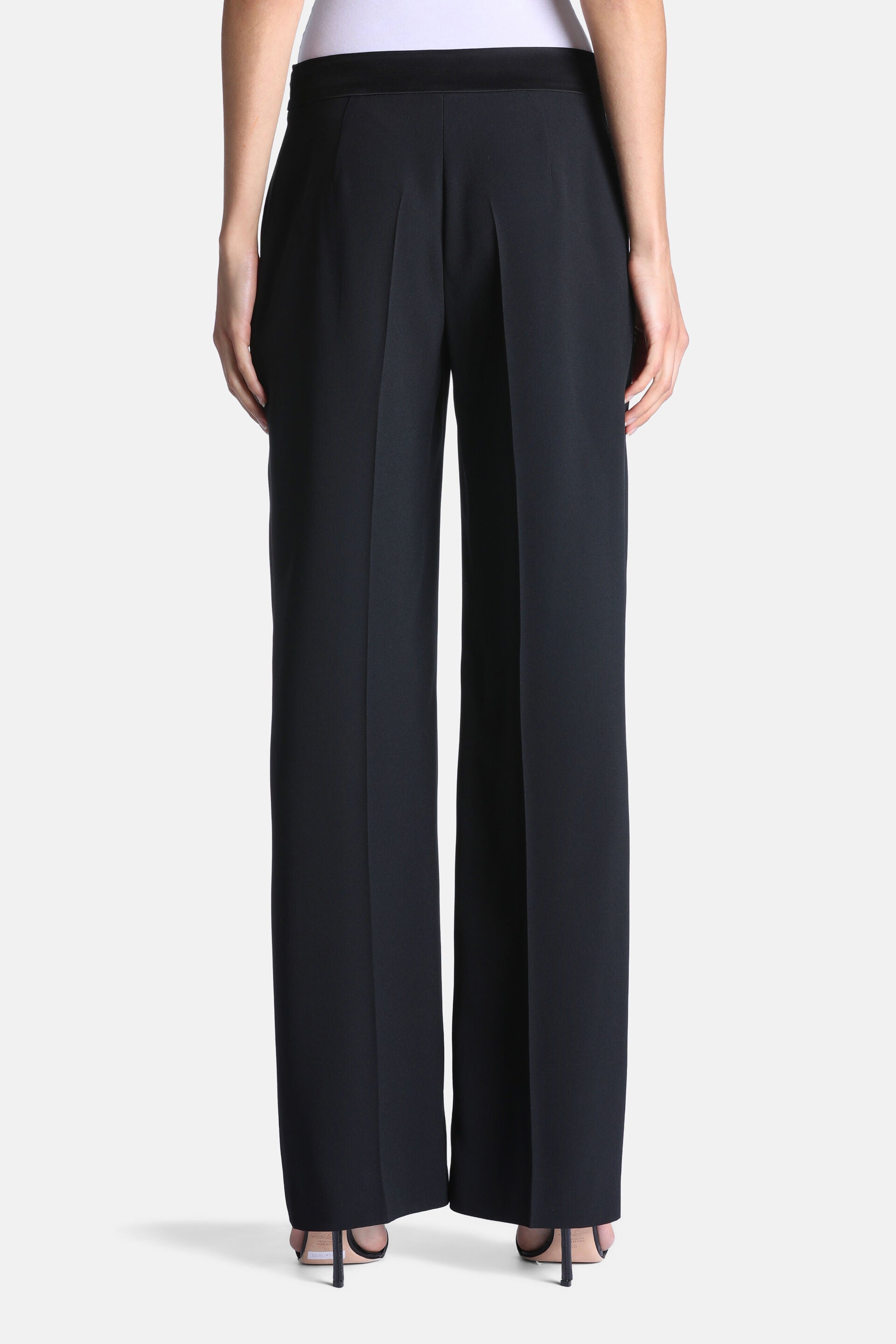 Black wide-leg trousers made of smooth fabric. Features a distinct black waistband and vertical creases down the center of ea