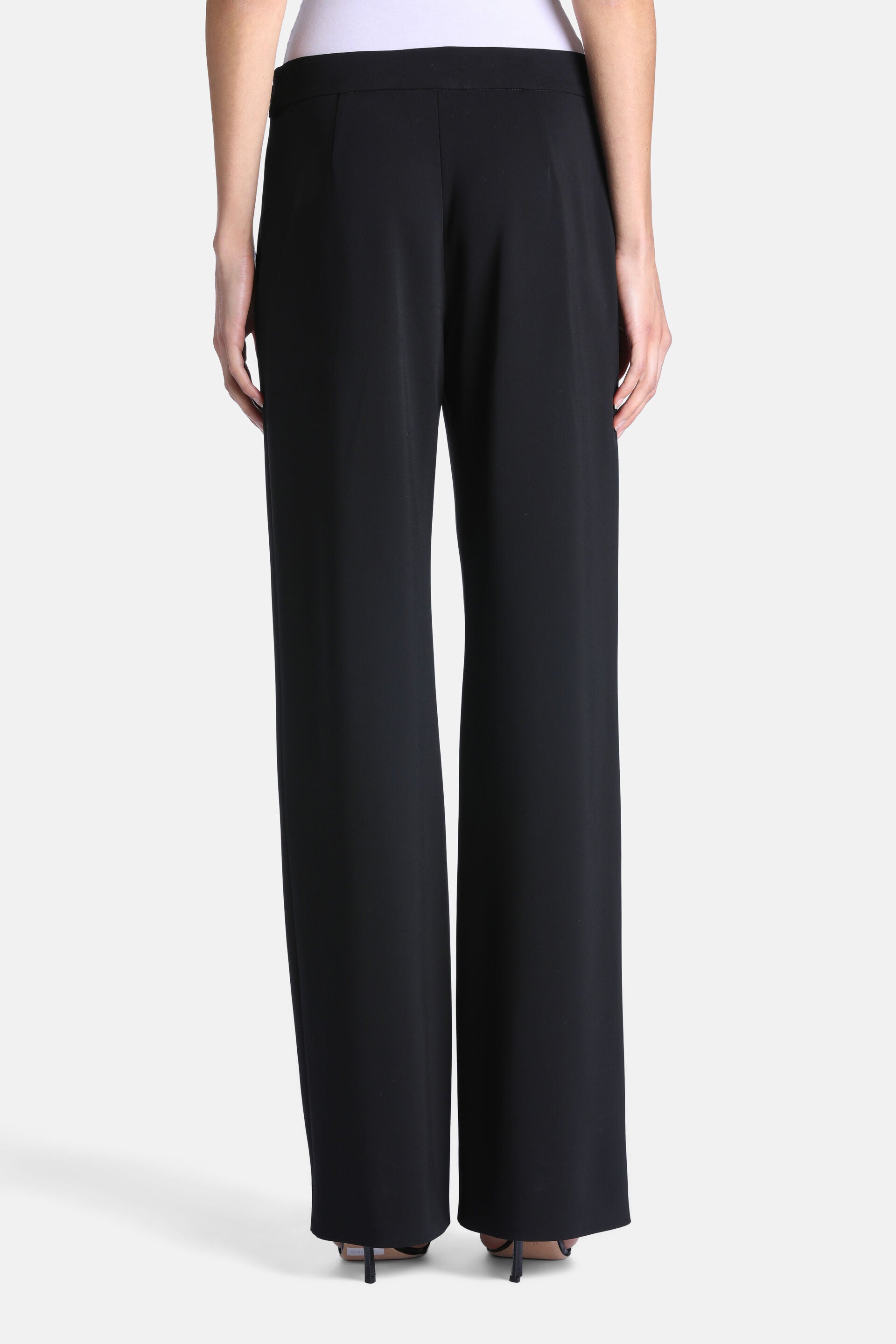 Black wide-leg trousers with a smooth, flowing material and a flat, wide waistband at the back. Long, wide hems.