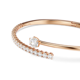 Rose gold-toned open bangle. One arm is solid, the other encrusted with clear crystals. A large clear crystal is prong-set on