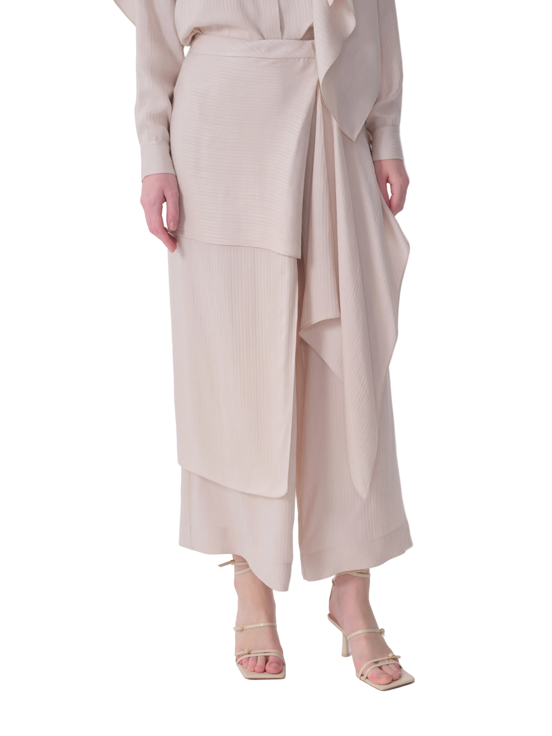 Light beige wide-leg cropped trousers with subtle vertical texture. Asymmetrical wrap design features a flat panel on the lef