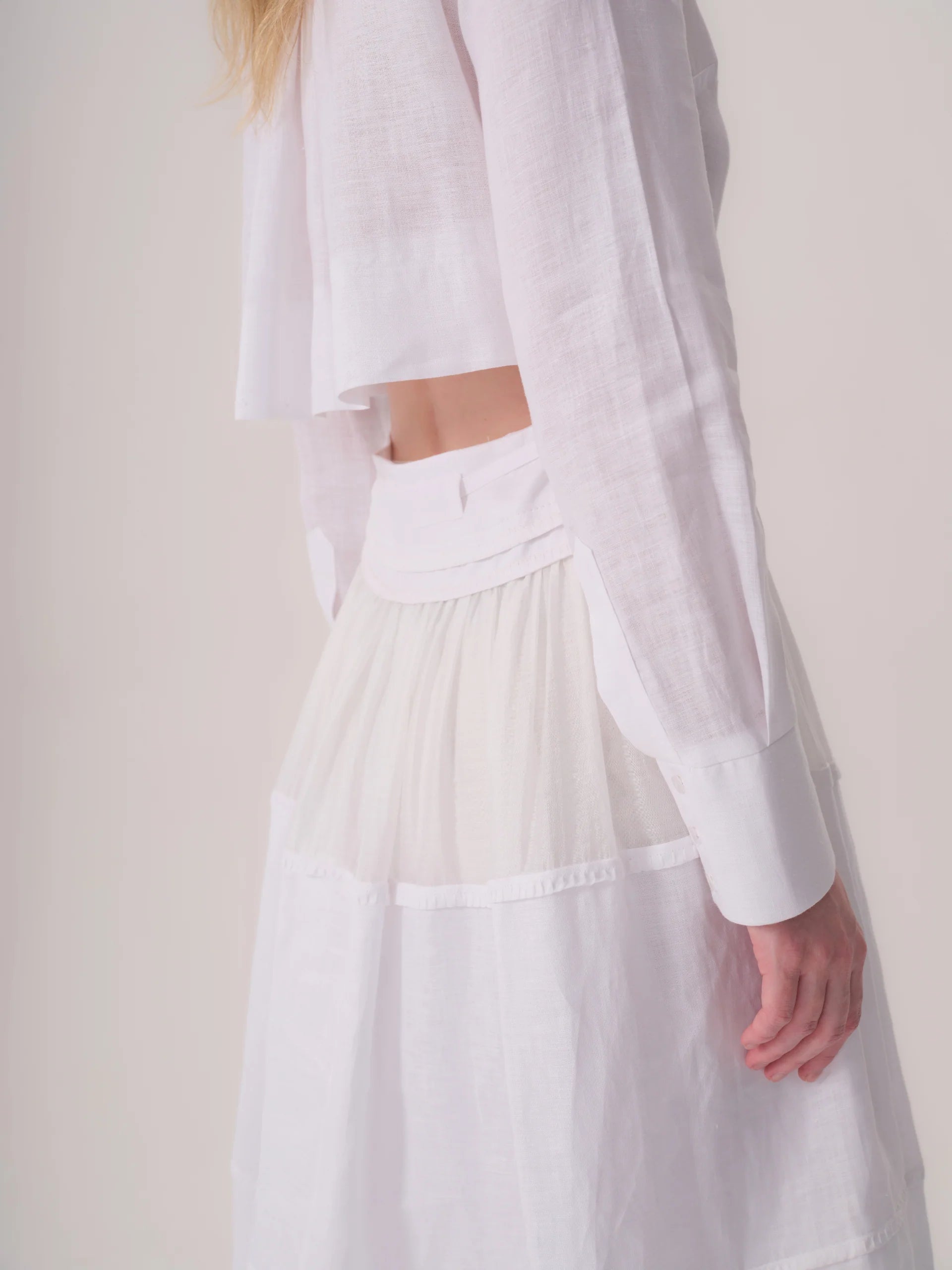 White dress in a light, textured fabric. Features a cropped long-sleeved top with a back cutout and a tiered, flowy skirt.