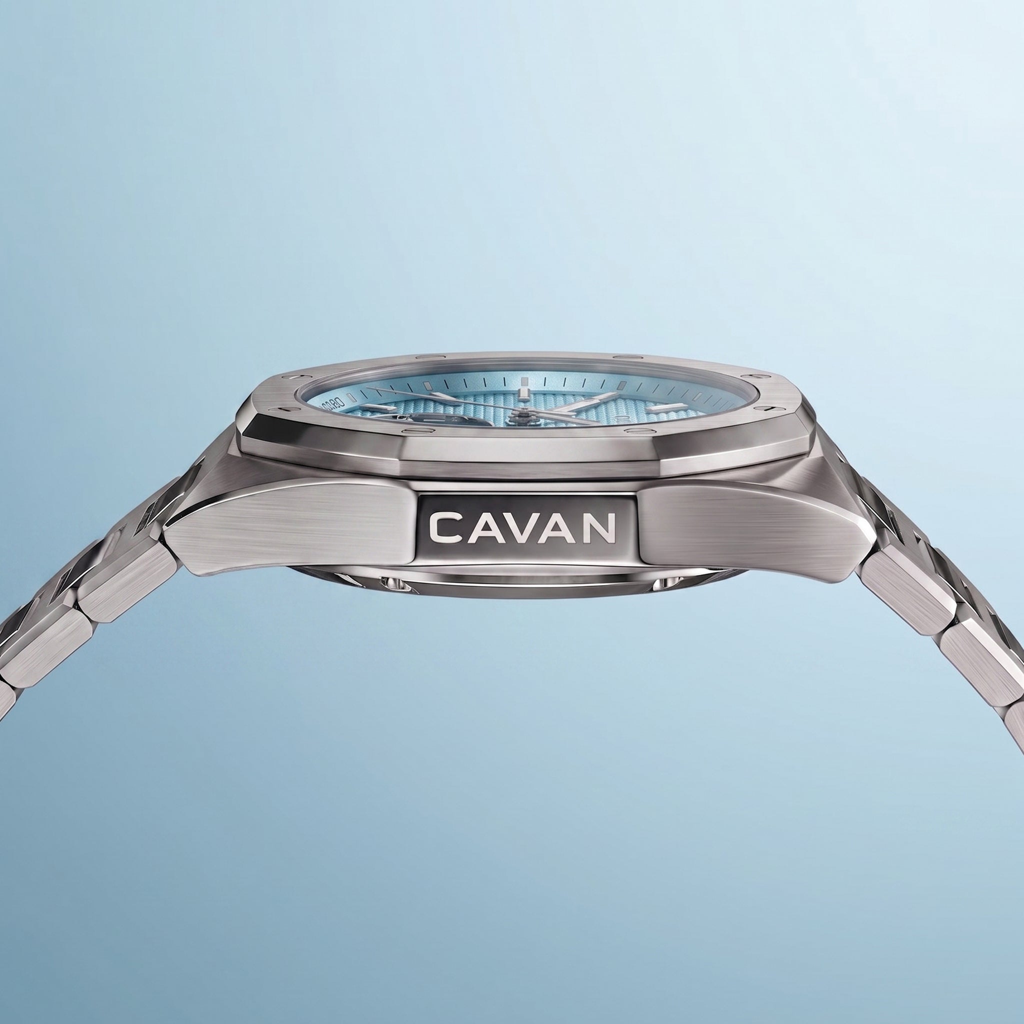 Silver-toned watch with an octagonal bezel, light blue textured dial, and a metal link bracelet. 'CAVAN' is engraved on the s