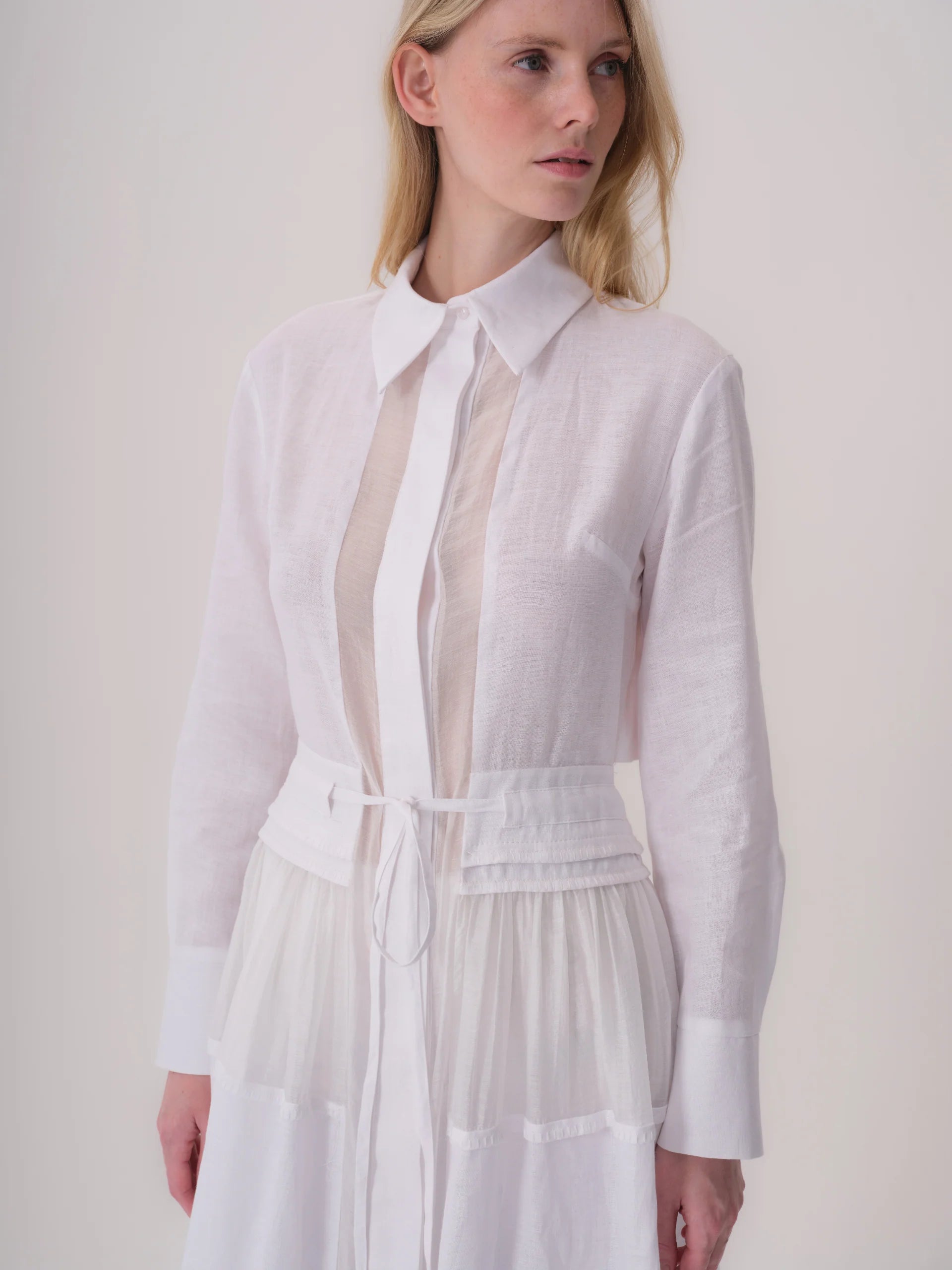 White collared dress with long sleeves, sheer front panel, tie-front waist with pleats, and tiered skirt.