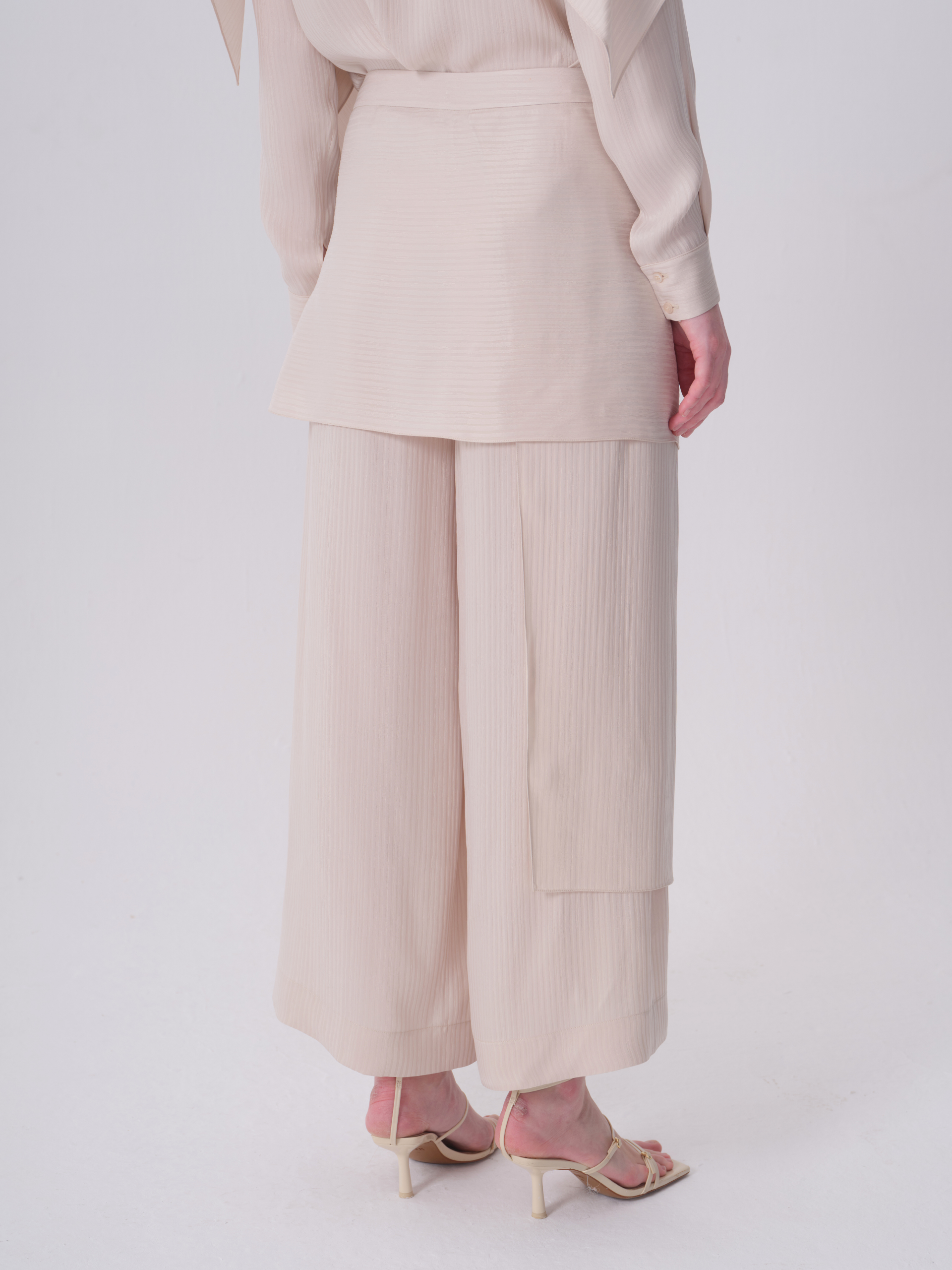 Off-white wide-leg trousers with a subtle vertical ribbed texture and a decorative flap panel on the right leg.
