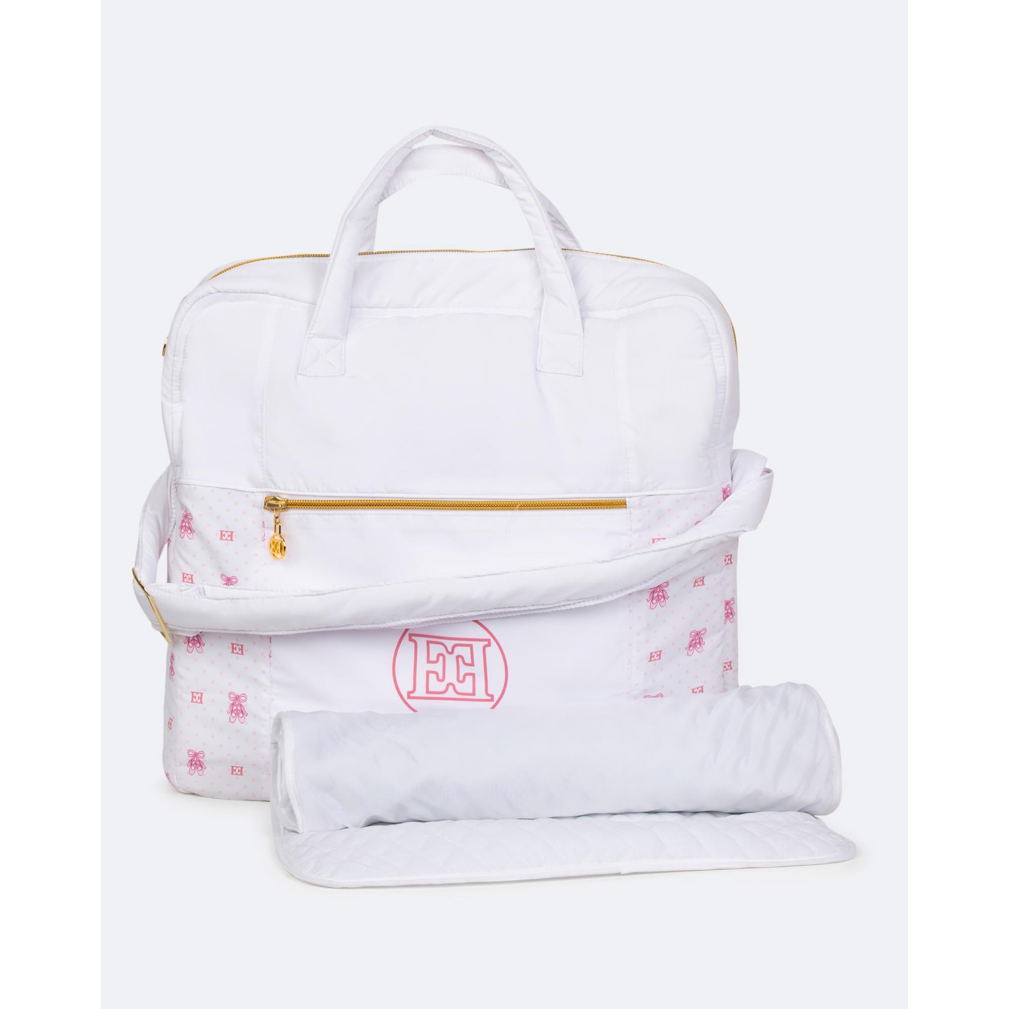 White changing bag with top handles, gold-toned zipper, pink ballet slipper pattern, and "EC" logo. Includes a white quilted