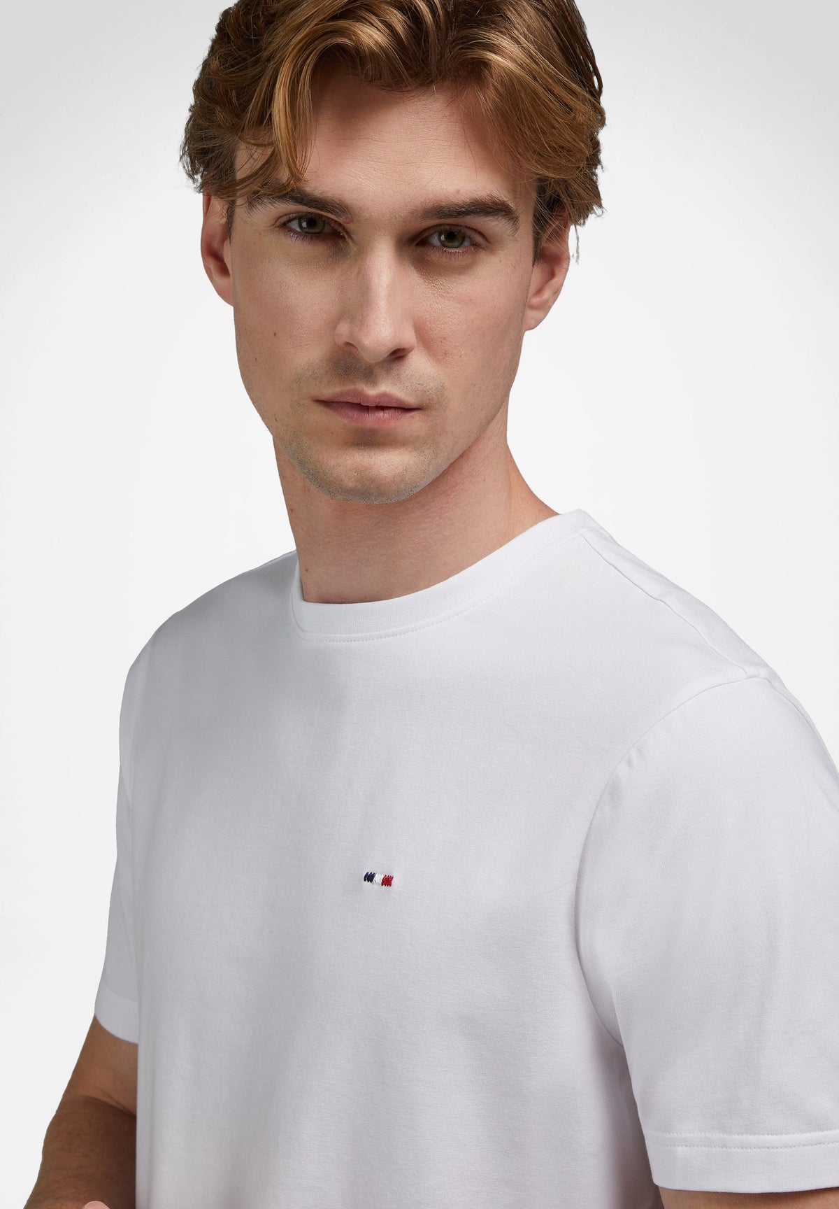 White short-sleeved crew neck t-shirt with a small embroidered white, blue, and red striped logo on the left chest.
