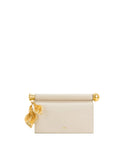 Light beige clutch with a gold-toned cylindrical top handle. Two gold-toned leaf charms hang from the left side. Gold-toned '