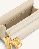 Open cream clutch bag with a smooth finish, an interior slip pocket, and a sculptural, wavy gold-toned metal handle.