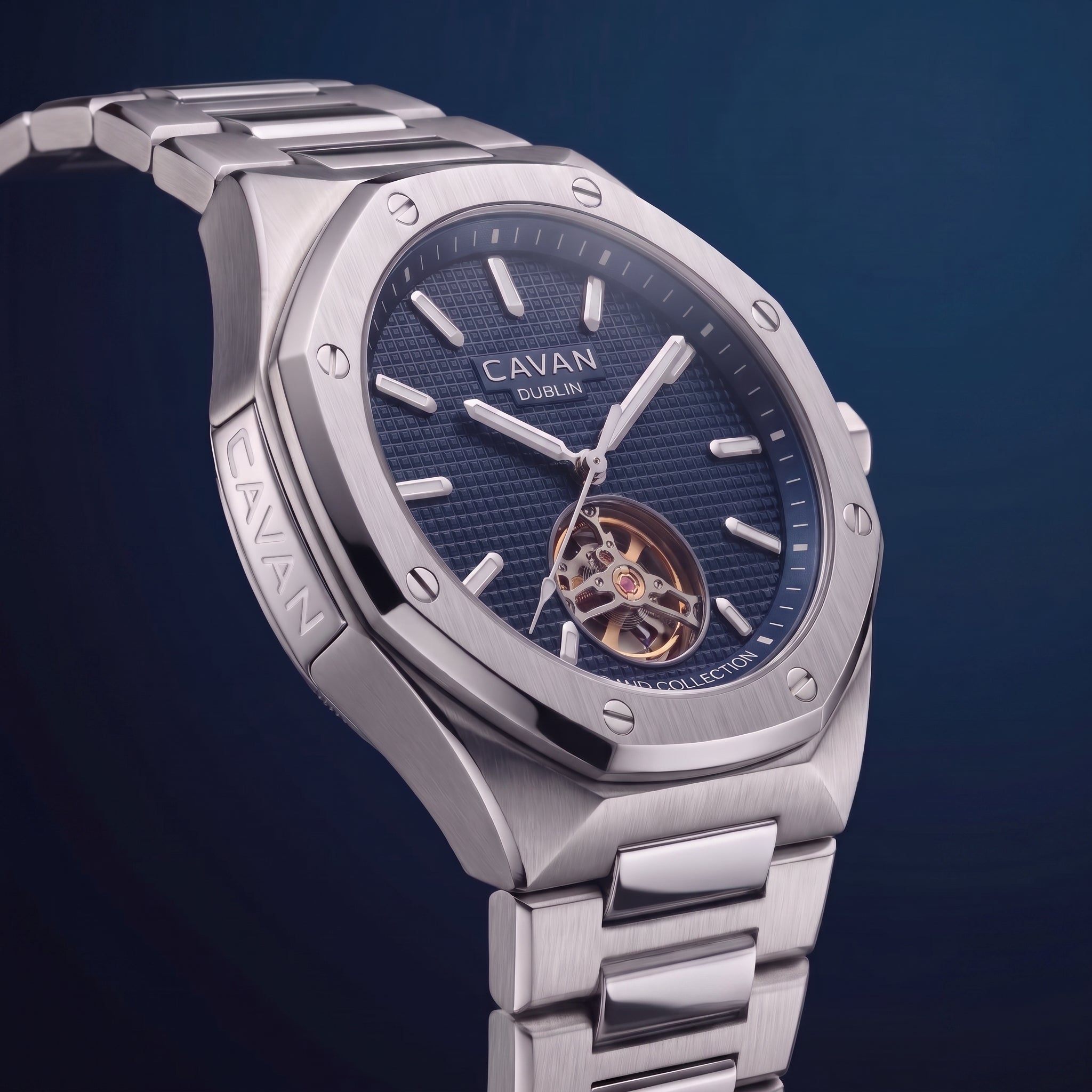 Silver-toned octagonal watch with a dark blue textured dial, open heart showing gold-toned gears, and a metal link bracelet.