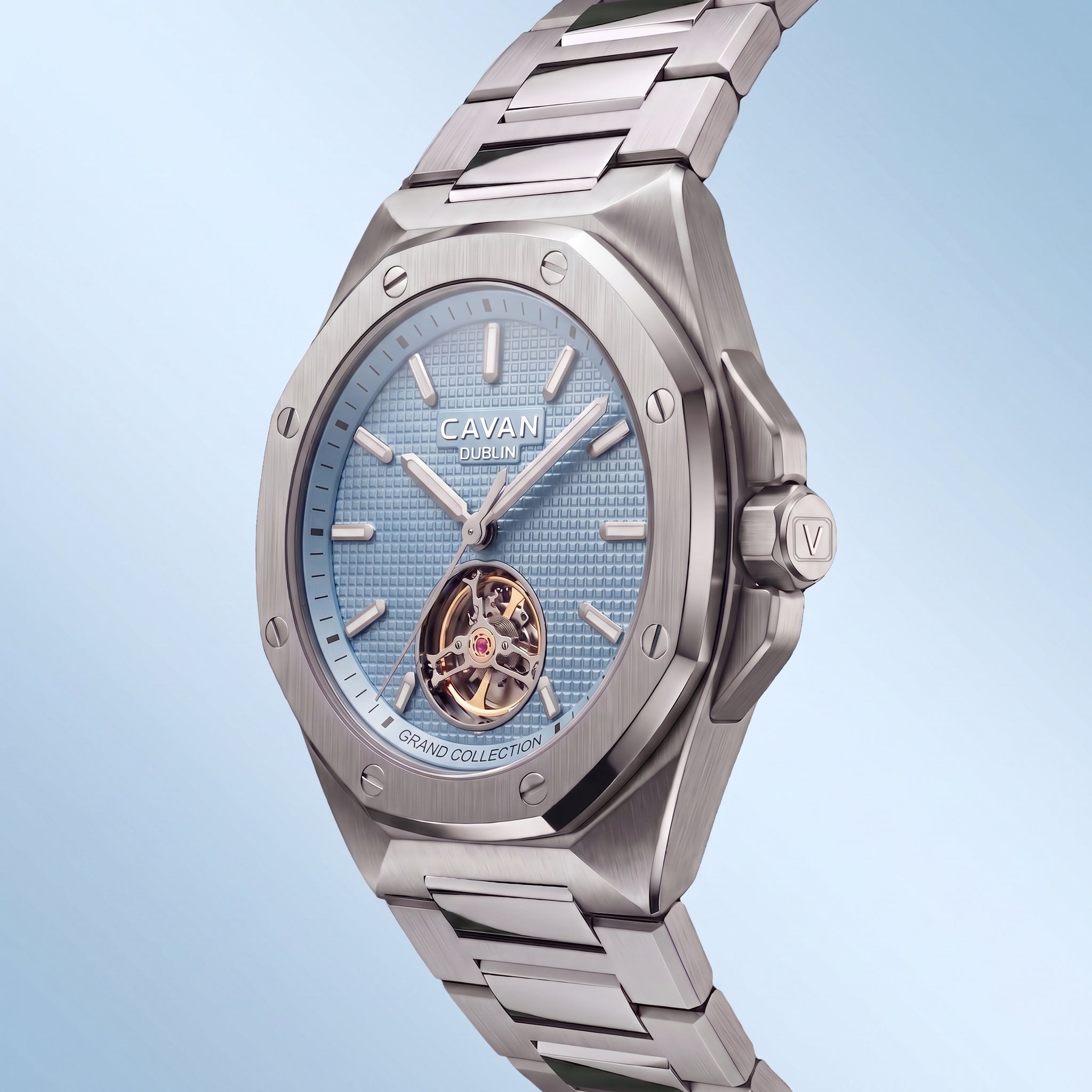 Silver-toned angular watch with a light blue textured dial, visible gold-toned mechanism at 6, and a metal link band.
