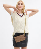 Woman wearing a cream cable knit vest over a white shirt, holding a brown handbag with a chain strap.