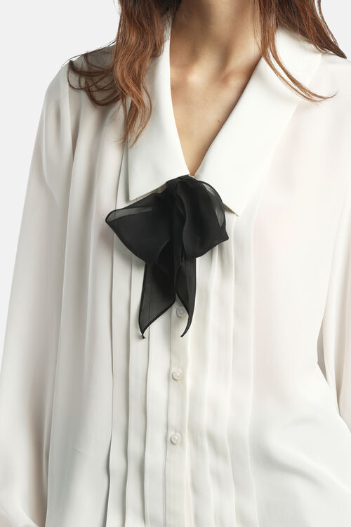 Off-white Crêpe de Chine shirt with a V-neck, pointed collar, and a black sheer bow. Features vertical pintucks and white but