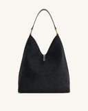 Black faux suede slouchy shoulder bag with a single black strap, gold-toned hardware, and a small black tab at the V-shaped o