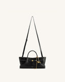 Black textured tote bag with short handles, a long adjustable strap with white stitching, a gold-toned buckle, and a dachshun