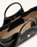 Black tote bag with white contrast stitching, spiraled handles, light brown lining, and a gold-toned rectangular charm.