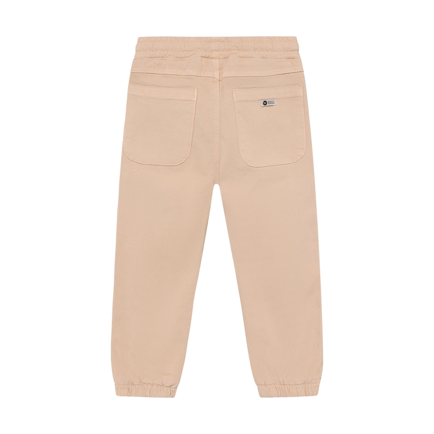 Back view of beige soft twill pants with elasticated waist, two patch pockets, and elasticated cuffs. Small label on left poc