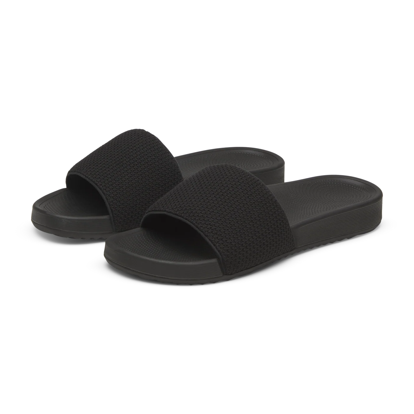A pair of black slide sandals with textured, woven-look straps and smooth, matte soles with ribbed sides.