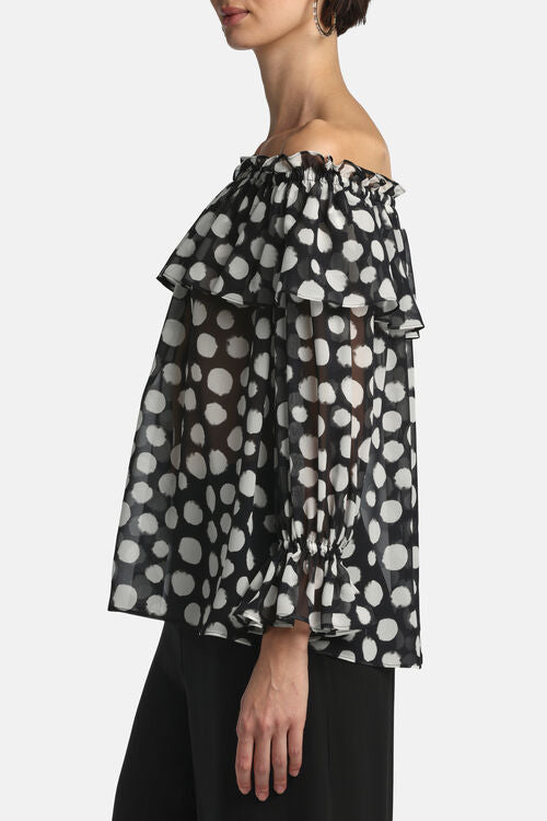 Sheer black off-shoulder blouse with white polka dots, ruffled neckline, and long sleeves with ruffled elastic cuffs.
