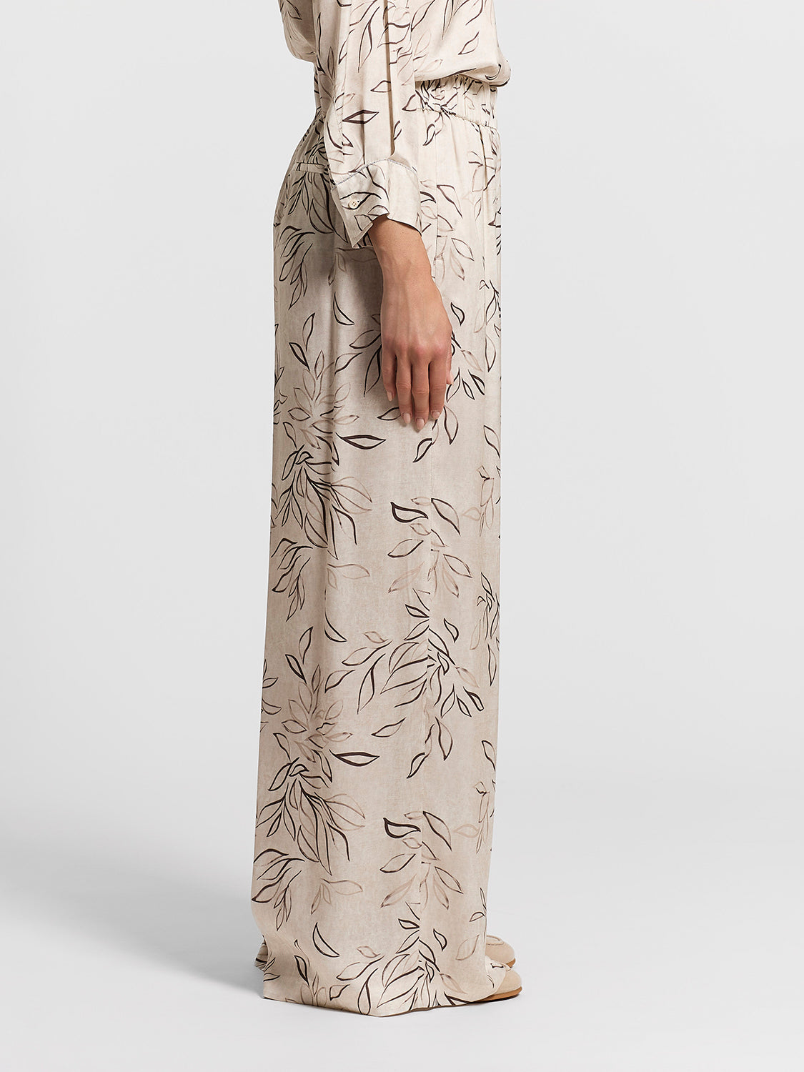 Beige wide-leg trousers with an all-over dark brown and light brown outline leaf pattern and an elasticated waist.