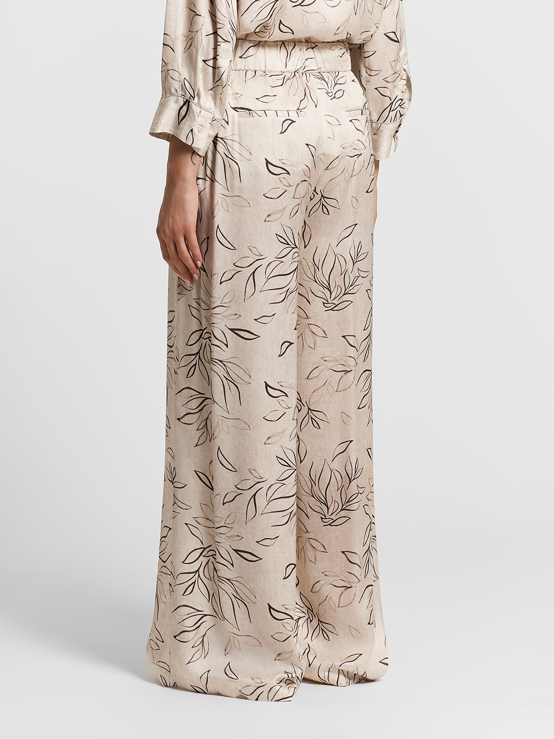 Beige wide-leg trousers with an abstract black and light brown leaf pattern, elasticated waist, and two back welt pockets.