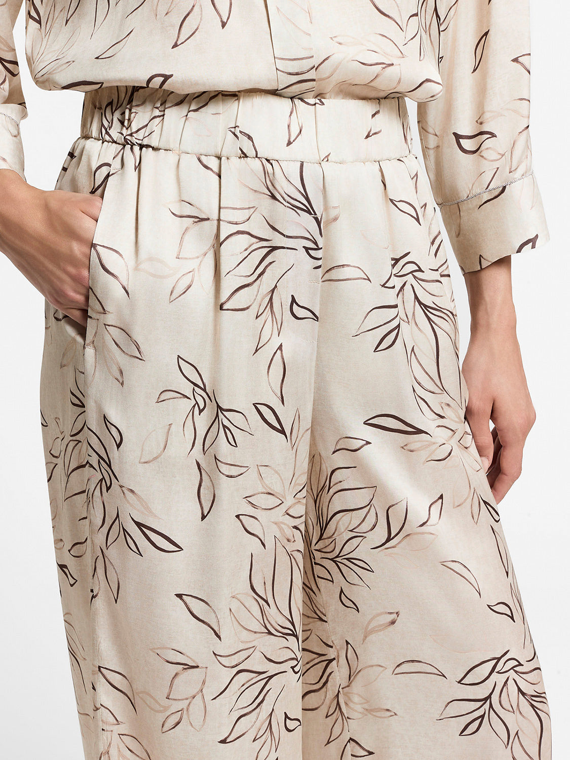 Beige wide-leg trousers with a subtle sheen, elasticated waistband, side pockets, and a brown abstract leaf pattern.