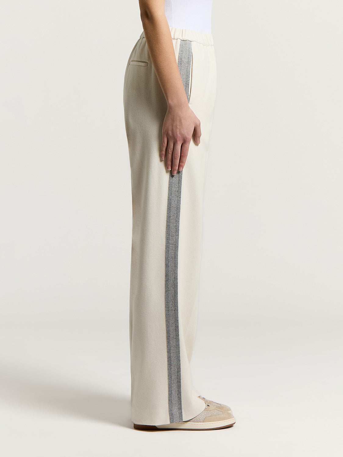Light beige wide-leg trousers with an elasticated waist, a horizontal slit pocket, and a shimmering grey vertical stripe down