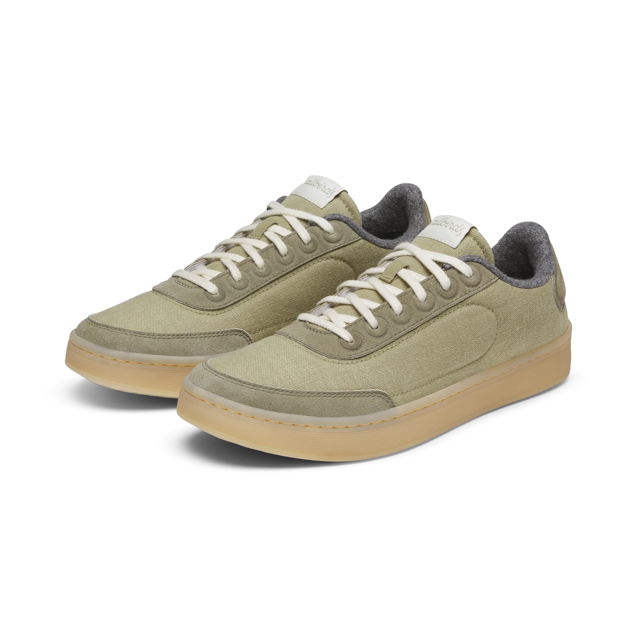 Pair of green canvas low-top sneakers with light green suede trim, white laces, grey felt collar, and translucent beige soles