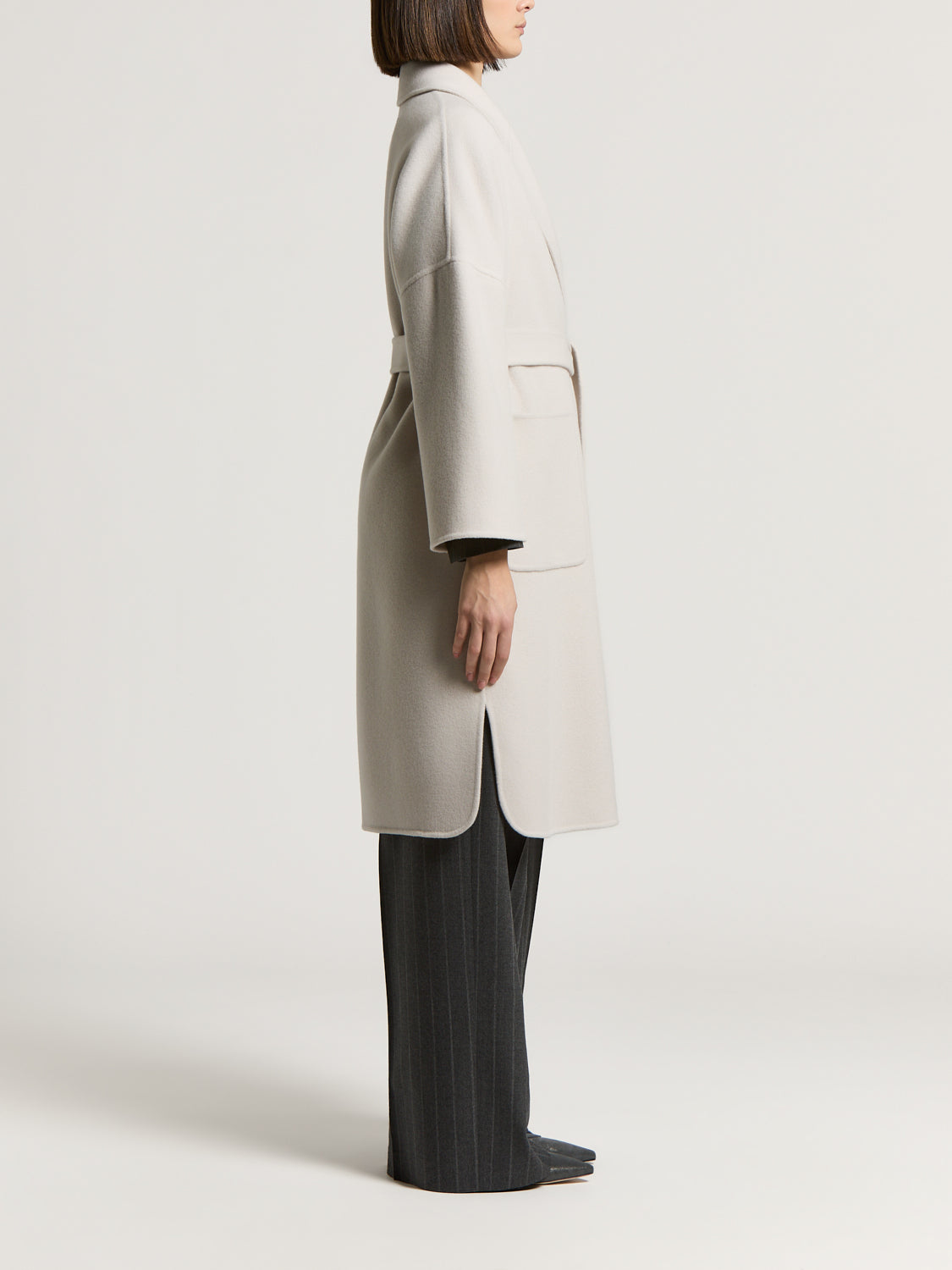 Icy beige long coat with wide lapels, a self-tie belt, and large front patch pockets. Side slits with rounded hems.