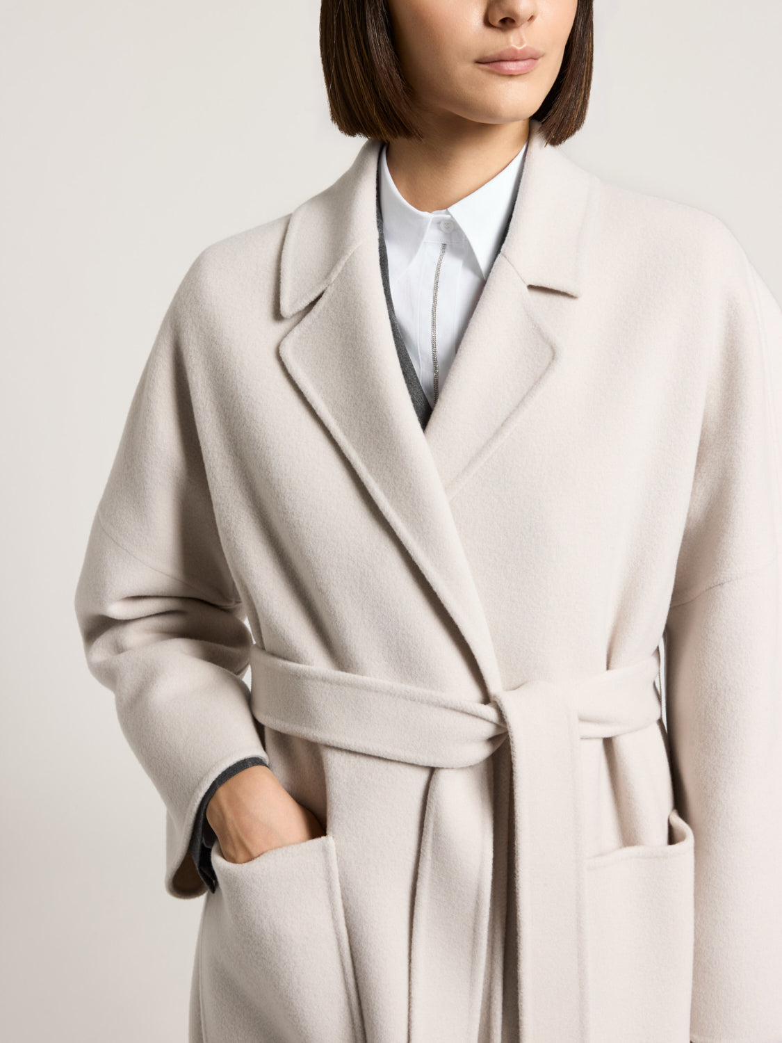 Icy beige wrap coat with wide notched lapels, long sleeves, a self-tie belt, and two large front patch pockets.