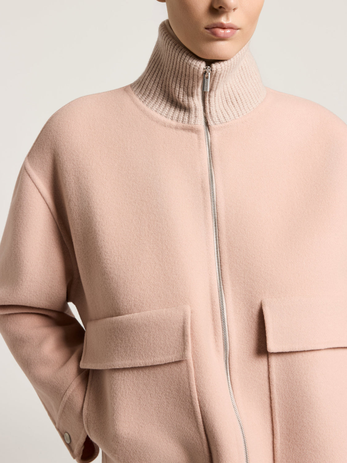 Light pinkish-beige coat with a cream ribbed turtleneck, silver-toned front zipper, and two large flap pockets.