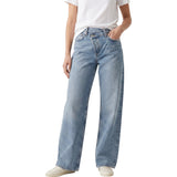 Full-length studio shot of a model wearing the Agolde criss-cross blue wide-leg jeans styled with a simple white t-shirt.