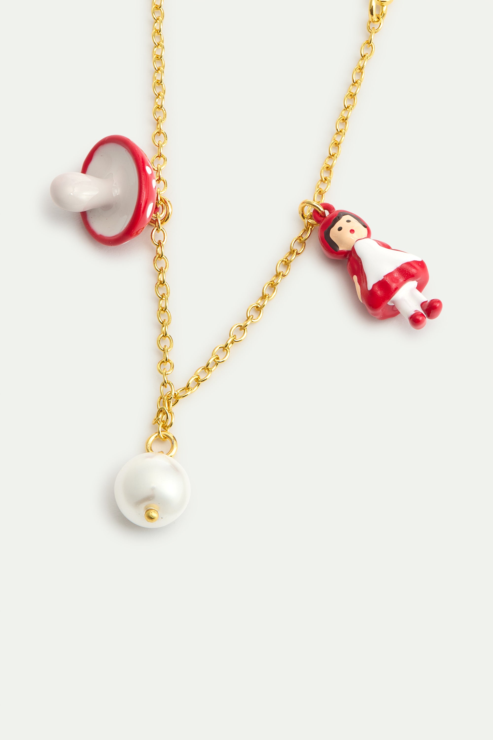 Gold-toned chain bracelet with three charms: a red and white pacifier, a small doll in a red dress, and a white pearl.