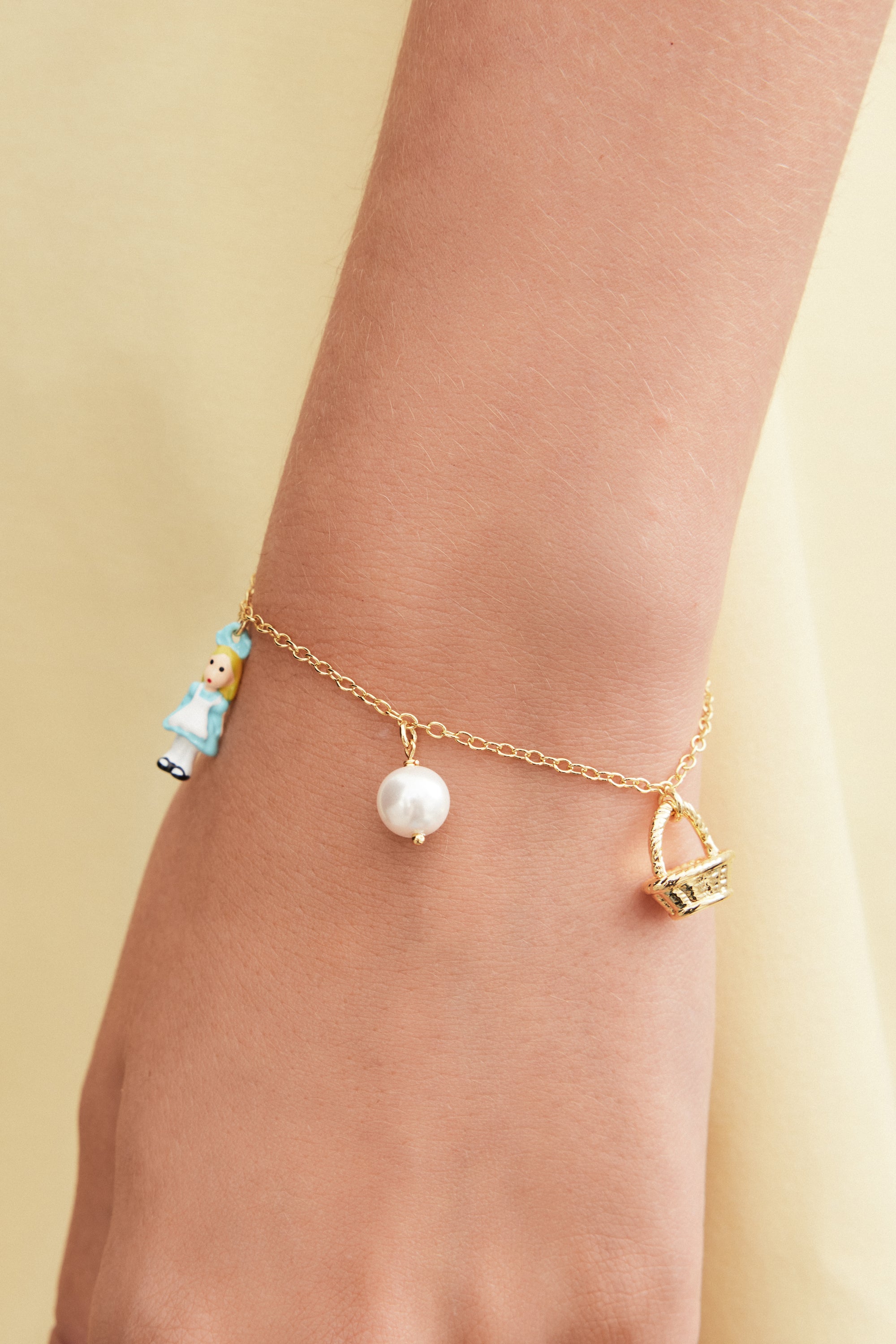 Gold-toned chain bracelet with three charms: a doll in a blue dress, a white pearl, and a gold-toned basket.