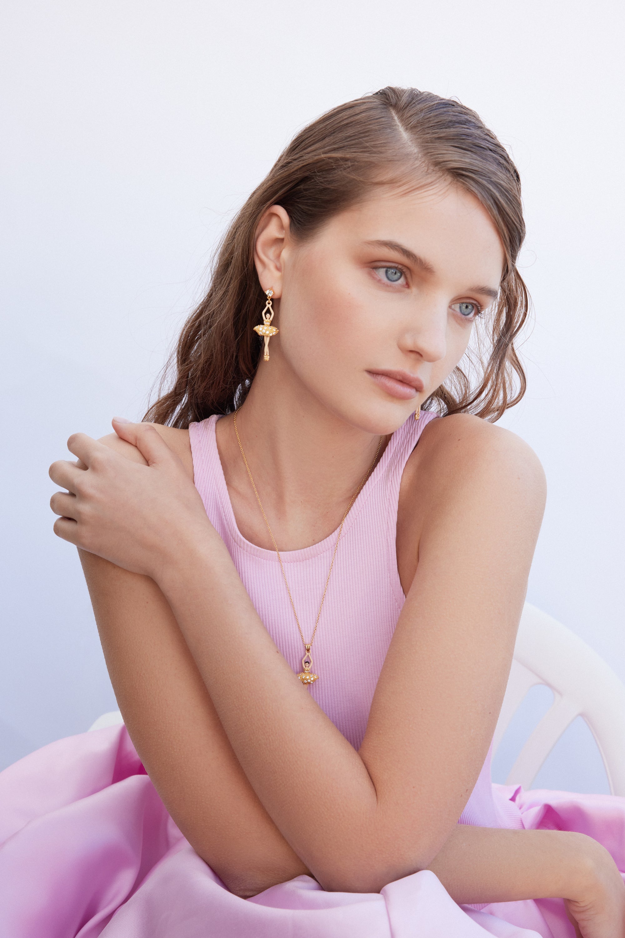 Gold-toned dangle earring featuring a clear gem stud, an infinity link, and a ballerina figure with a textured tutu.