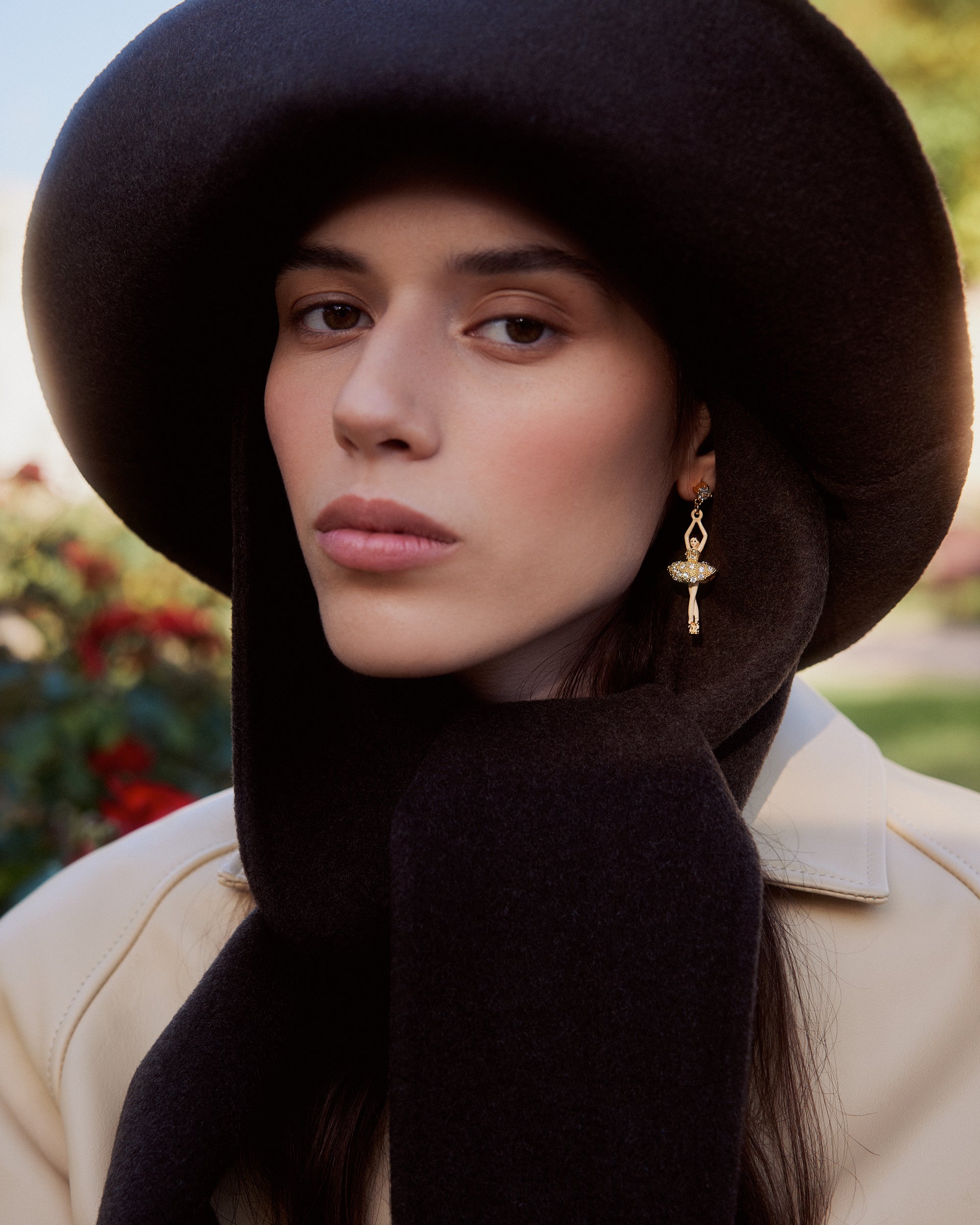 Gold-toned dangle earring with a crystal-adorned ballerina figure in a tutu, hanging from a small dark stud with a gold-toned