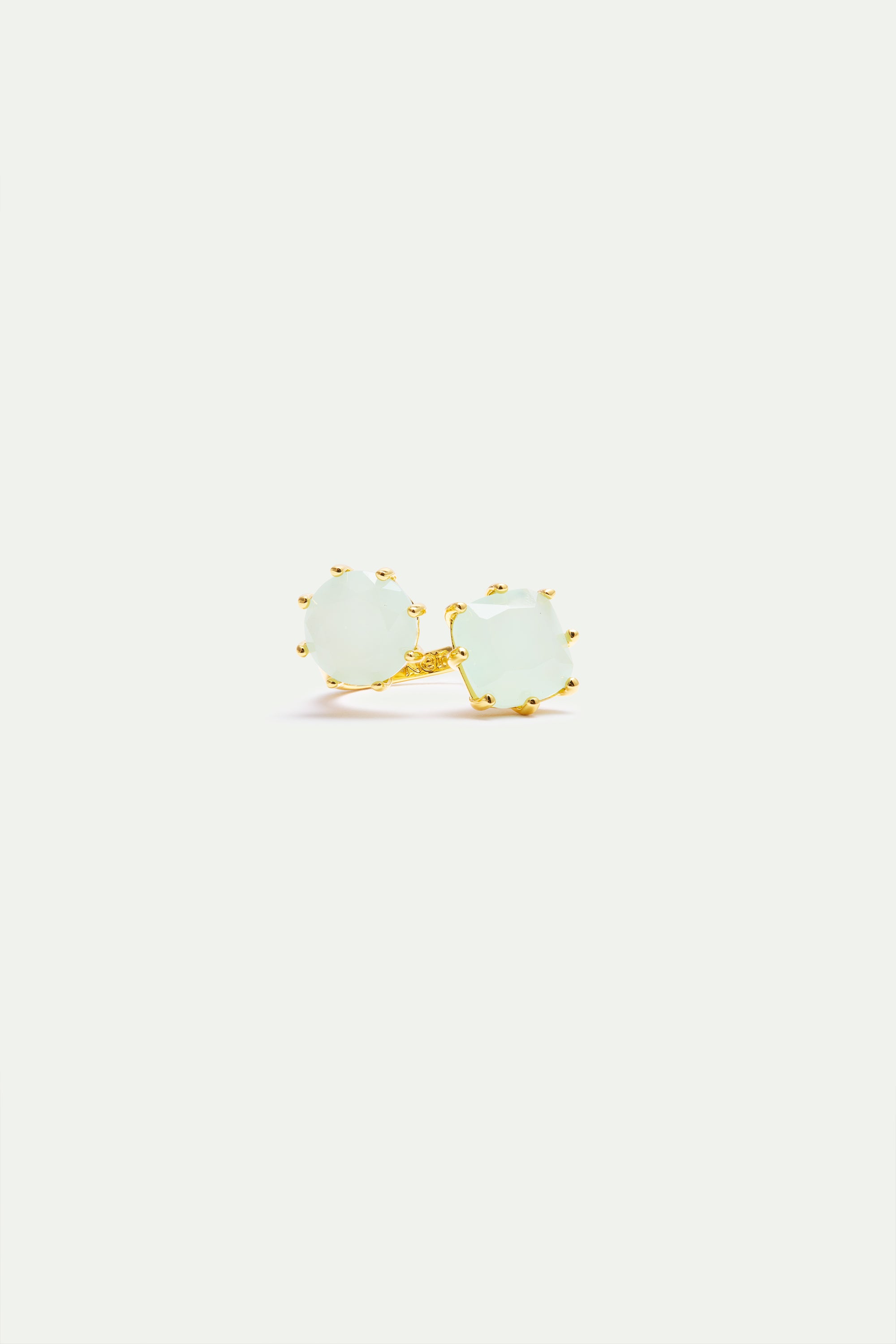 Adjustable ring with two light green, irregularly shaped, faceted stones set in gold-toned prongs on a gold-toned band.